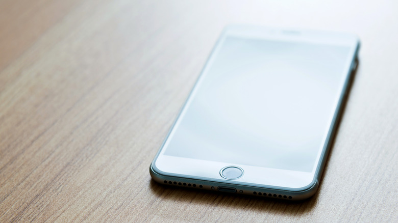 An iPhone 7 Plus on a desk, with the home Button highlighted by reflecting light.