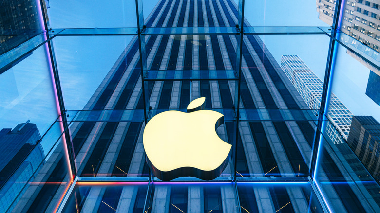The Apple logo against glass with a skyscraper looming in the background