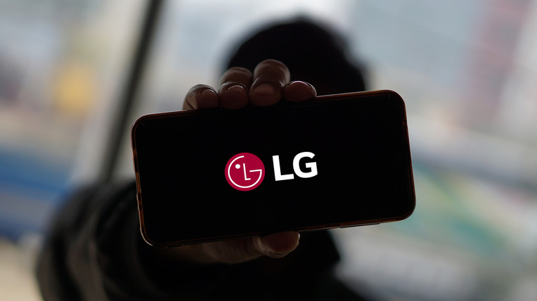 Person in shadow holding up an LG smartphone with its logo on the screen.