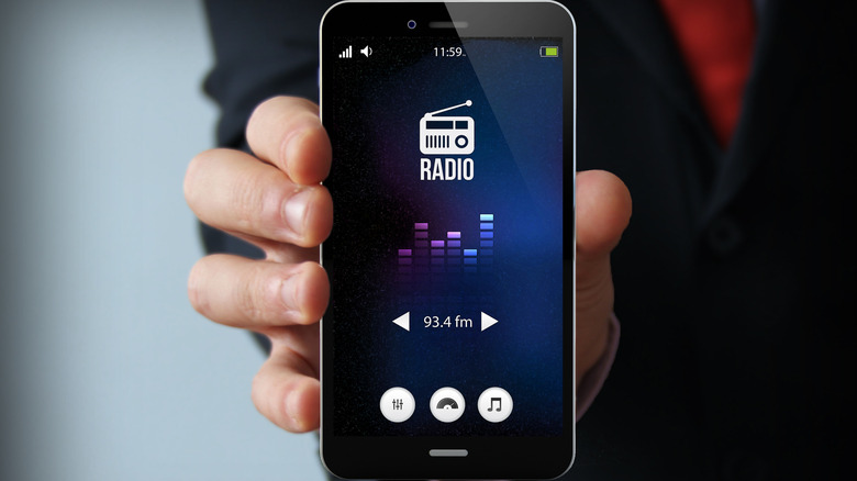 An FM radio app shown on a smartphone's screen while a person holds the device.