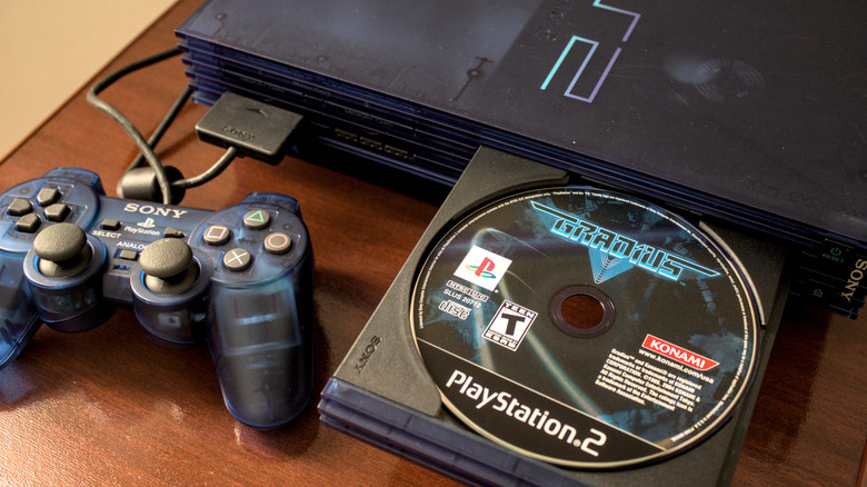 PlayStation 2 with a controller and opened disc tray with a disc inserted in