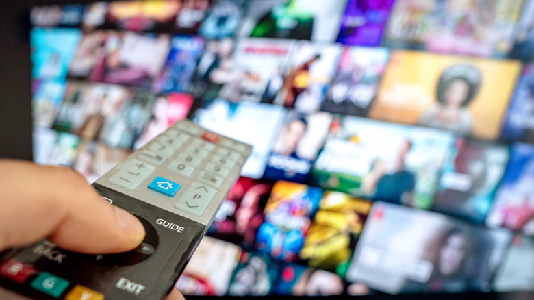 hand using a remote, smart TV with video and show icons blurred in background