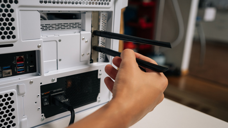 A person installing two Wi-Fi antennas to the back of a desktop computer