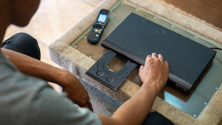 Someone getting ready to use a DVD player with a flip phone nearby