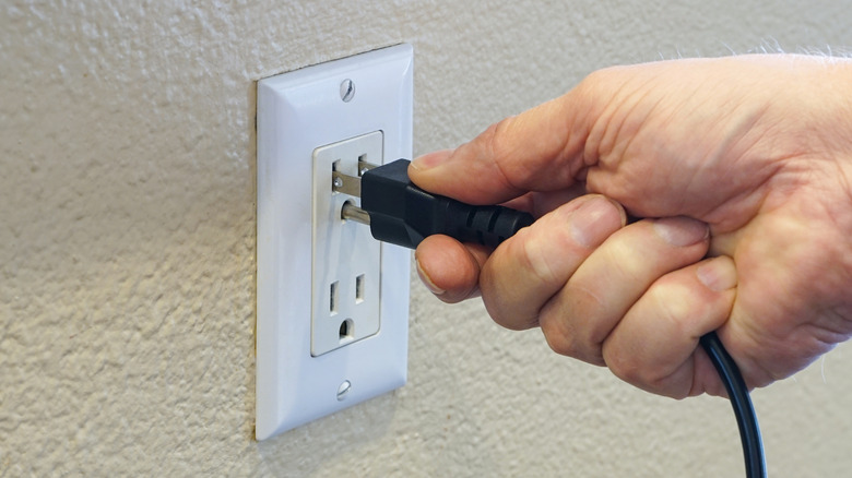 Hand plugging a polarized power cord into a wall electrical outlet