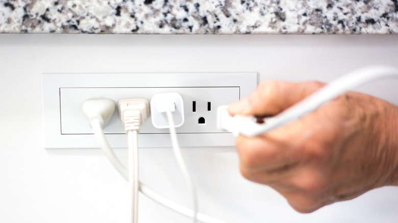 Hand holding a polarized power plug near a wall outlet with other devices already connected