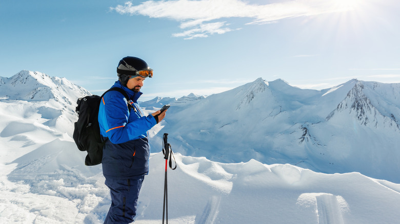 Skier using a smartphone in the cold mountains with snow.