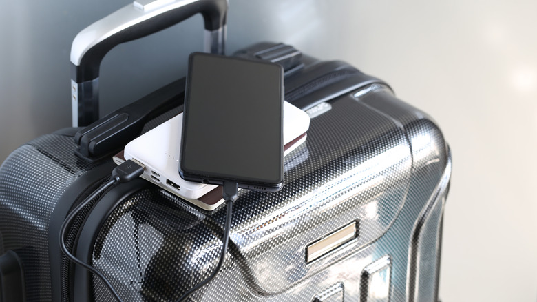 Power bank plugged into a smartphone and resting atop luggage.