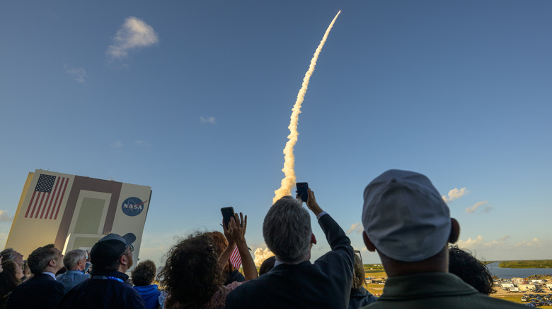 A crowd watching Artemis II's launch. The rocket is flying at a curve.