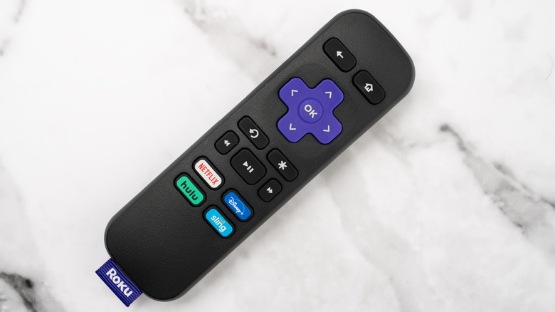 A Roku remote on a table with the purple tag visible on the bottom.