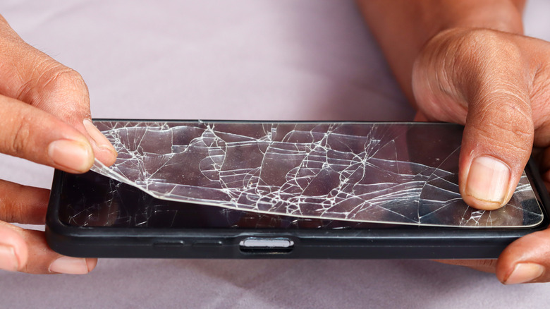 Person removing a cracked tempered glass screen protector.