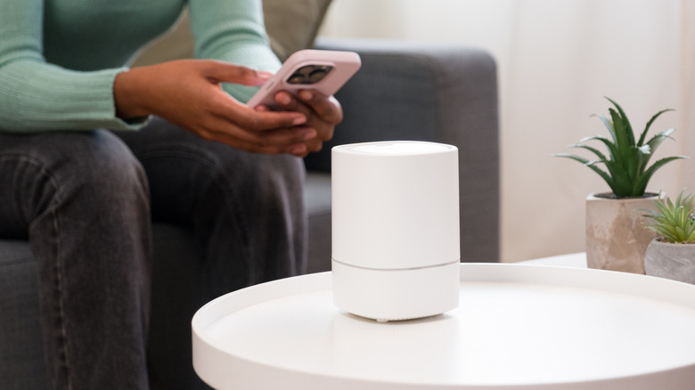 A person sitting in front of a smart home device and holding a smart phone.