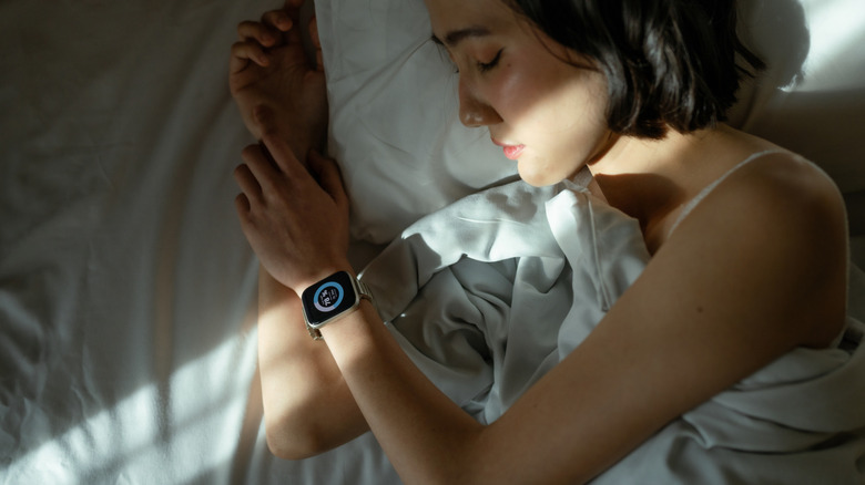 A person sleeping in bed with smartwatch on their wrist, with the screen on tracking sleep cycles.