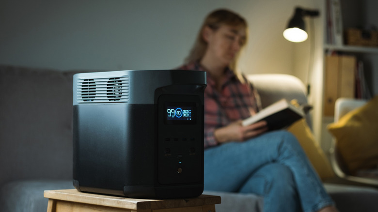 EcoFlow power station in the foreground with woman reading a book by night light behind.