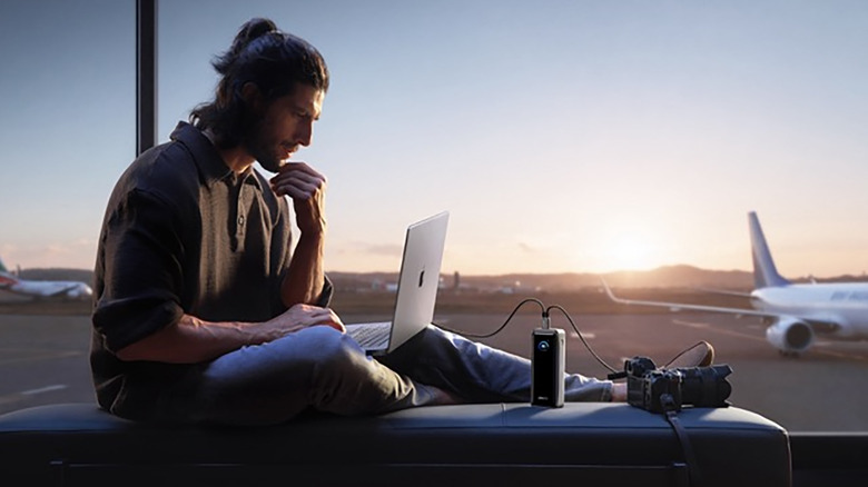 A man by the window at an airport on his laptop connected to an Anker charger.