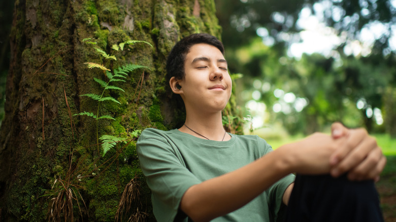 Someone listening to earbuds sat under a tree.