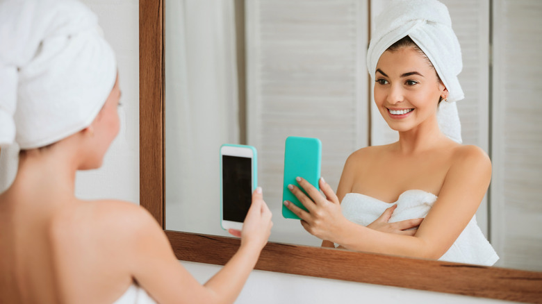 A woman points her smartphone toward a bathroom mirror.