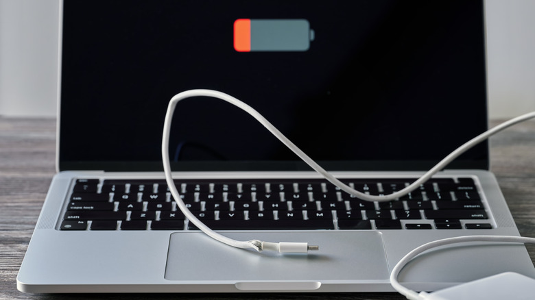 A silver MacBook with a whit, frayed USB-C cable laying on top of it, the MacBook screen shows a low battery icon