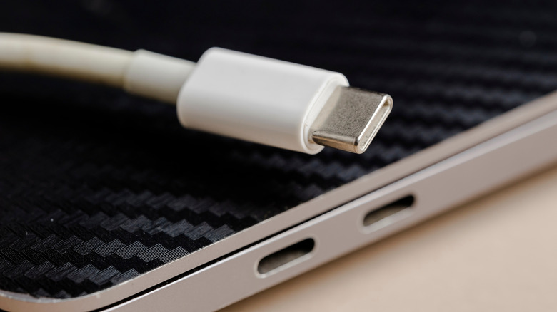 A photo focusing on two USB-C ports on a laptop while also showing a white USB-C cable sitting on top of the device, suggesting the USB cable will help charge the device