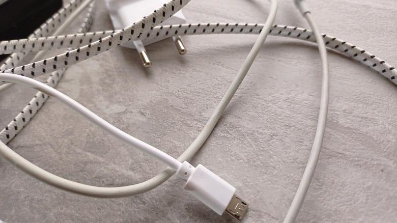 A phone charger surrounded by different USB cables with differing cord material against a light-colored backgroun