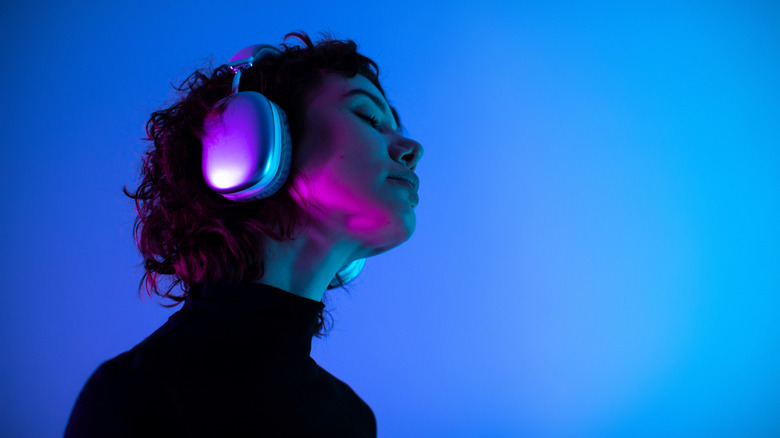 Someone listening intently to over-head headphones with a neon glow background.