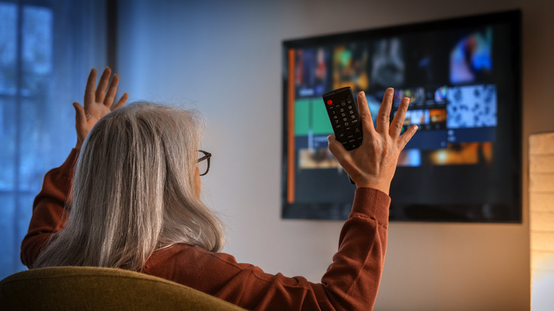 women sitting on a chair holding a remote frustrated with the TV in front