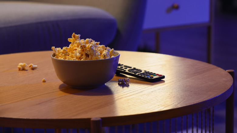 A TV remote on a table next to a bowl of popcorn