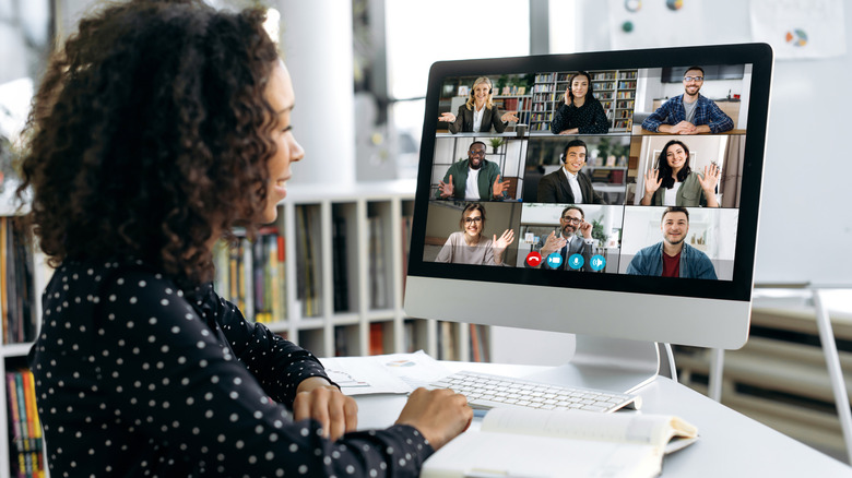 A woman smiling at her desktop computer with a nine person video call on her screen