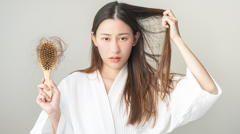 A woman is holding up a hairbrush where lots of her hair has fallen off