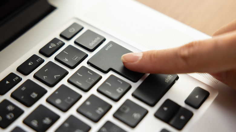 A finger pressing the Enter key on a keyboard.