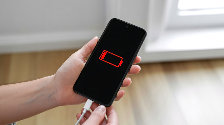 A person holding a phone connected to a charger, showing a low battery symbol