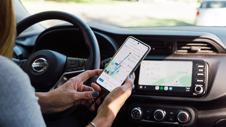A person sitting behind the wheel of a car using Google Maps on her phone.