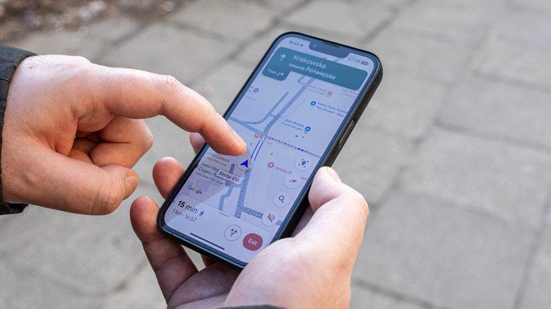 Two hands holding a phone on the street using Google Maps.