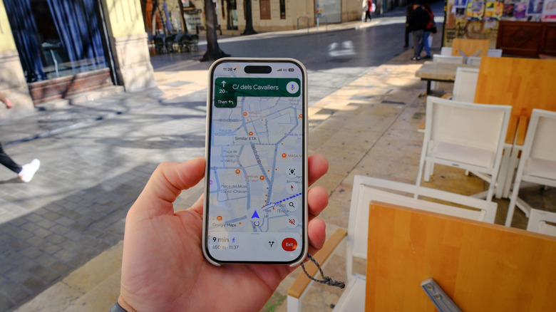 A hand holding a phone by an outdoor patio with Google Maps directions on screen.