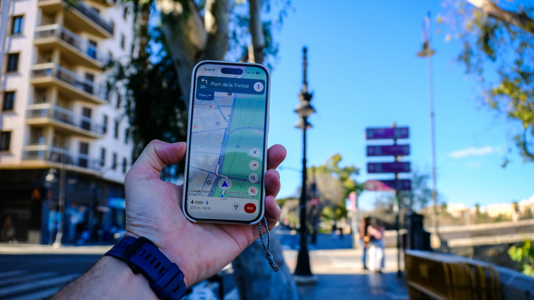 A person on a sidewalk holding a smartphone with Google Maps showing directions