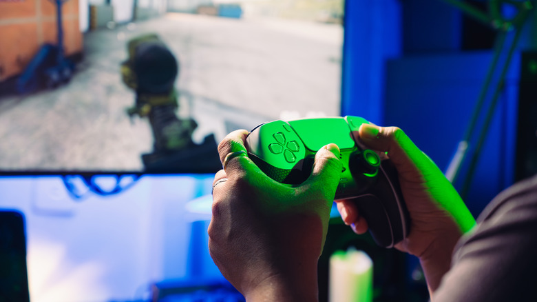 Someone playing a PS5 with DualSense controller in hand and game on TV.