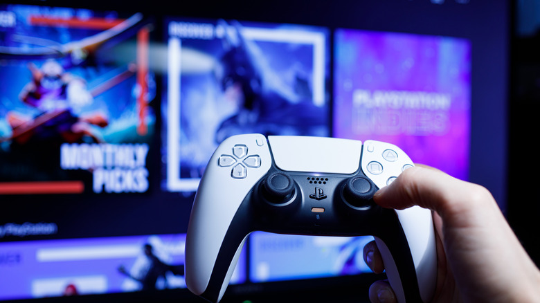 PS5 DualSense controller held up to screen with menus in background.