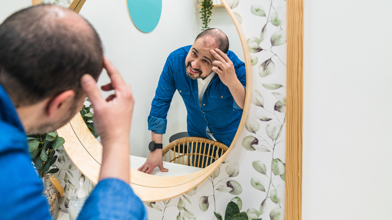Man going bald looking at his hair in a mirror
