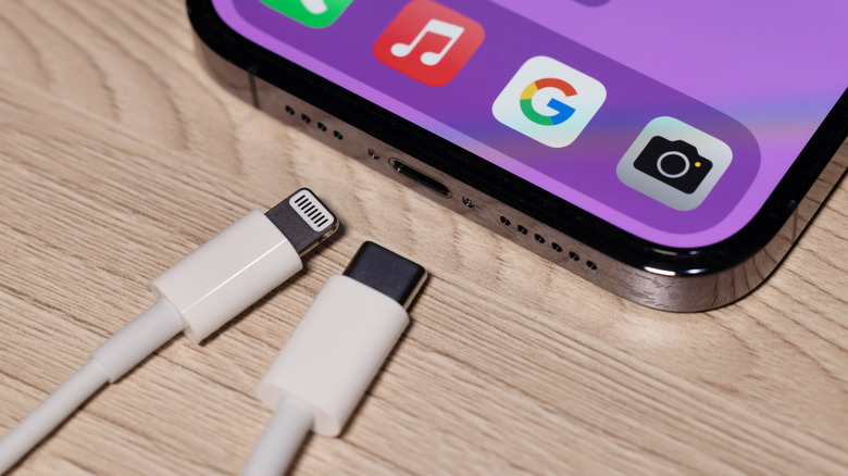 A lightning connector and a USB-C connector lying in front of an iPhone displaying its port