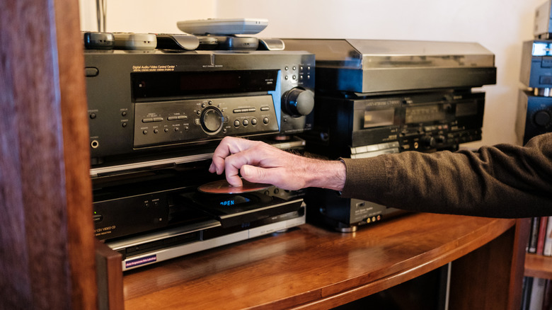 Someone loading CDs and DVDs into classic players and equipment on a shelf.