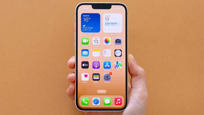 Hand holding an iPhone 16E on a beige background