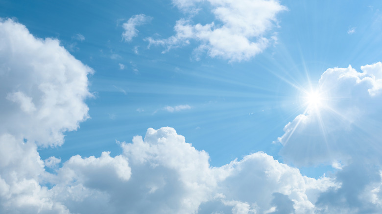 The sun peaking behind scatterings of fluffy grey and white clouds