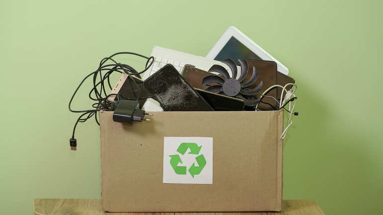 A cardboard box with a recycling logo on the side holding old electronics.
