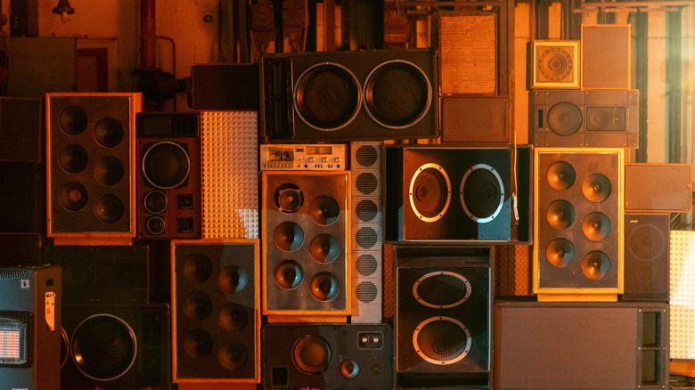 A wall of various box-style speakers bathed in orange light.