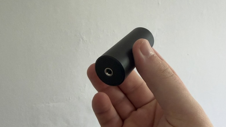 A black ground loop isolator being held in someone's hand with a white wall in the background.