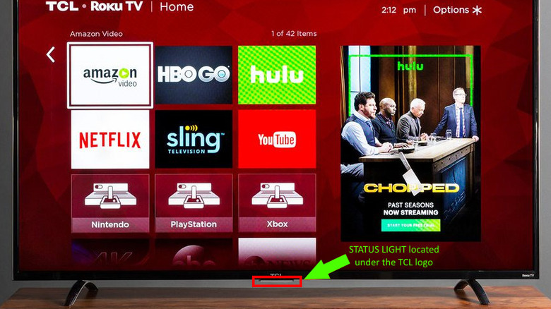 A TCL TV placed on a TV stand. A red square highlights its status light, located under the TCL logo.