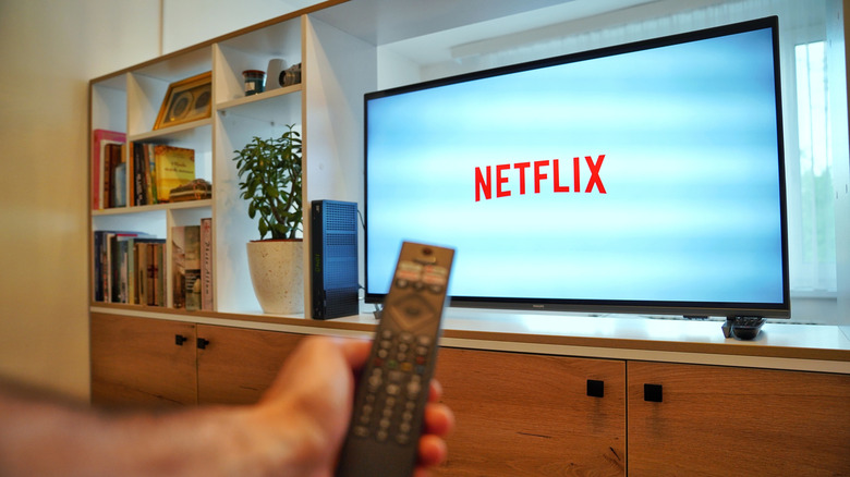 A person holding a remote control up to a TV displaying the Netflix logo.