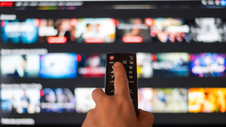 A person pointing a remote control at a TV displaying the Netflix home page.