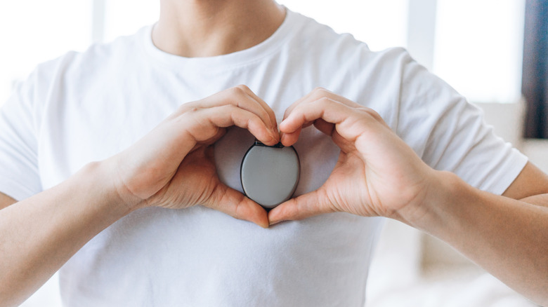 person holding pacemaker in hands with heart shape over chest