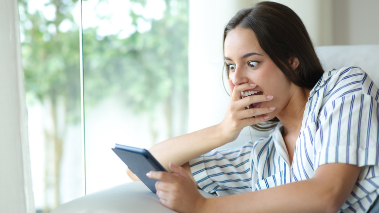 Woman showing a shocked face as she reads on an e-reader